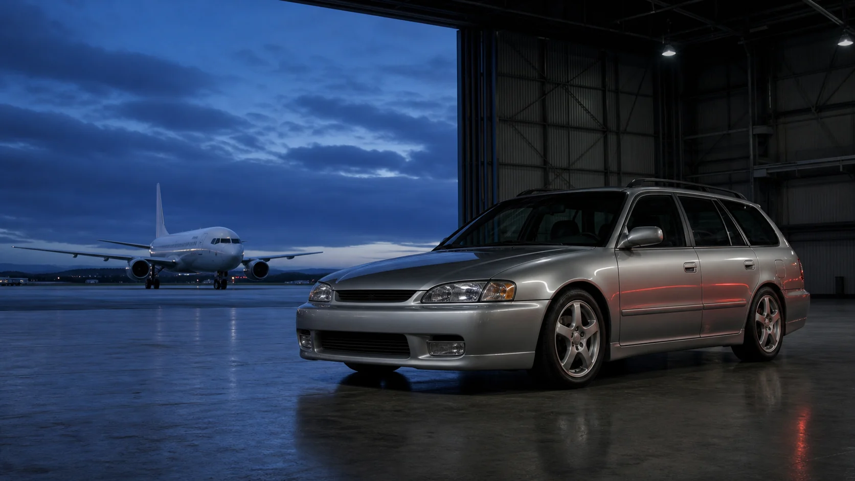 Silver sport wagon inside an aircraft hangar with a passenger jet in the distance